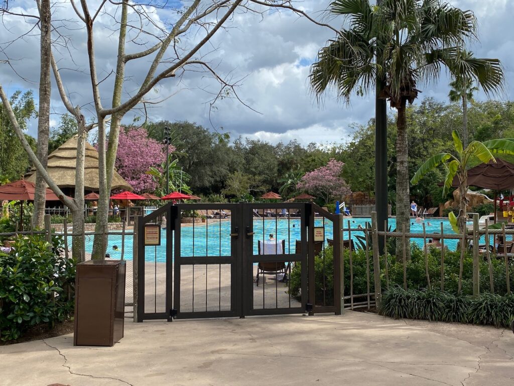 Concrete patio with large black metal gate in front of a large resort pool.