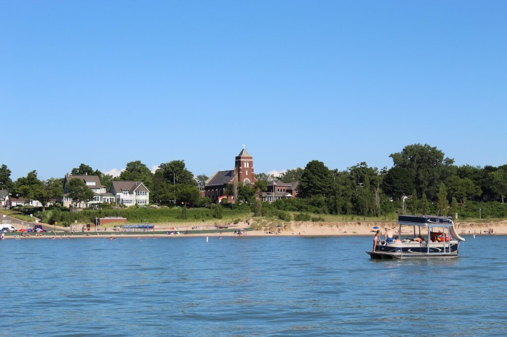 view of South Haven Beach with pontoon boat on lake, sandy beach, trees and a brick church
