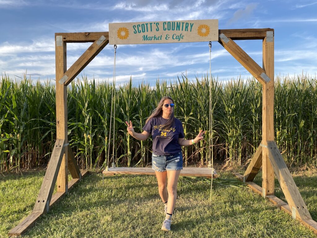 woman walking away from large wooden swing holding arms up making peace signs