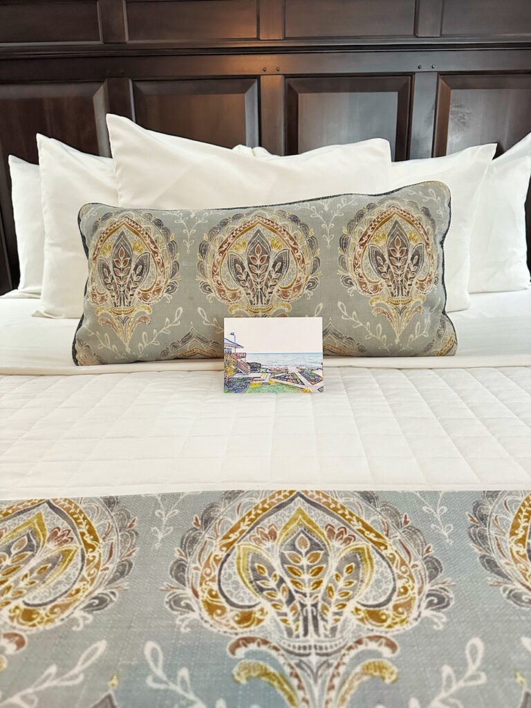 three fluffy pancakes with a lemon wedge on top and silver creamer cup of syrup on a white plate and a wood serving platter